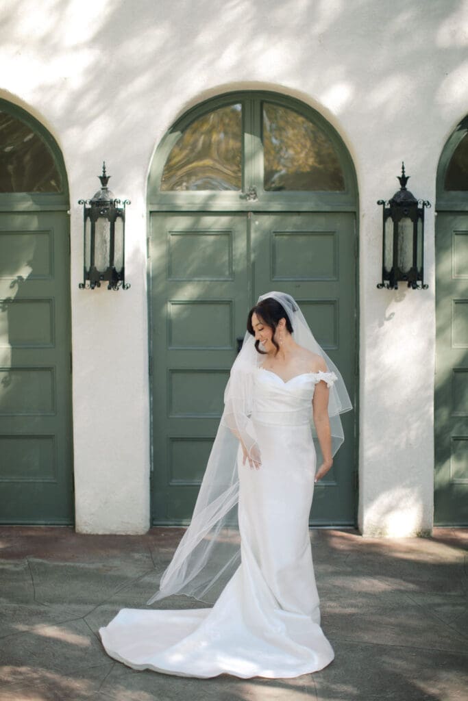 Bride standing in front of green doors looking down toward her right shoulder