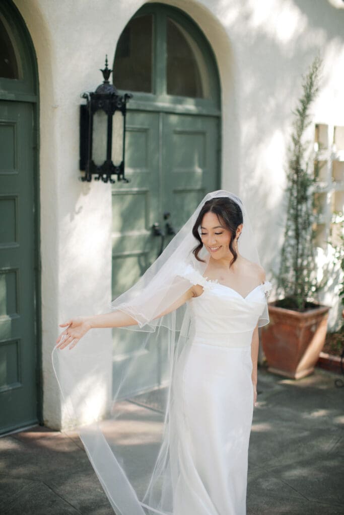 Bride smiling off to her right as she lifts up her veil