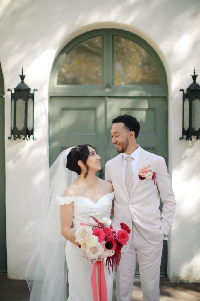 Bride and groom smiling at each other while bride holds pink and white wedding bouquet