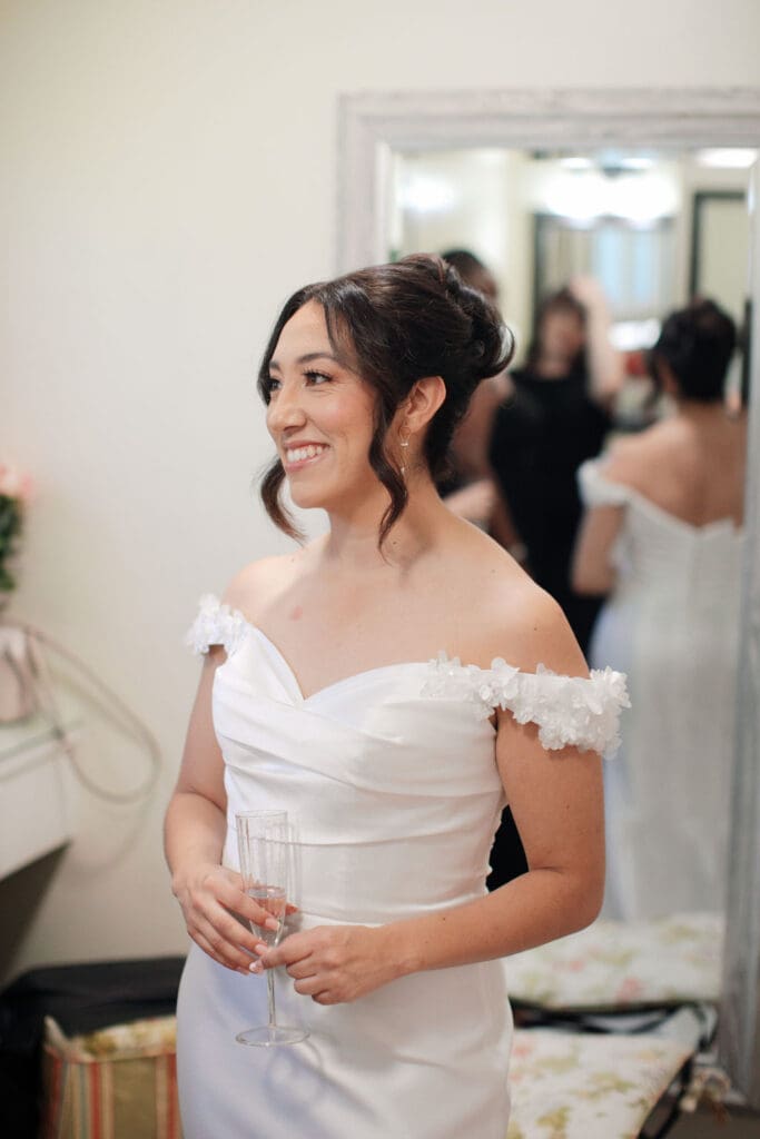 Bride smiling toward Pacheco Beauty team holding a glass of champagne