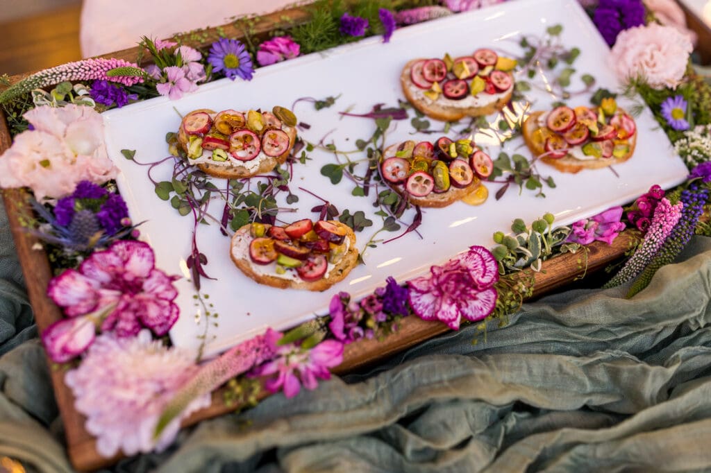 Elegant hors d'oeuvres on crostini topped with grapes and pistachios, framed by vibrant flowers.