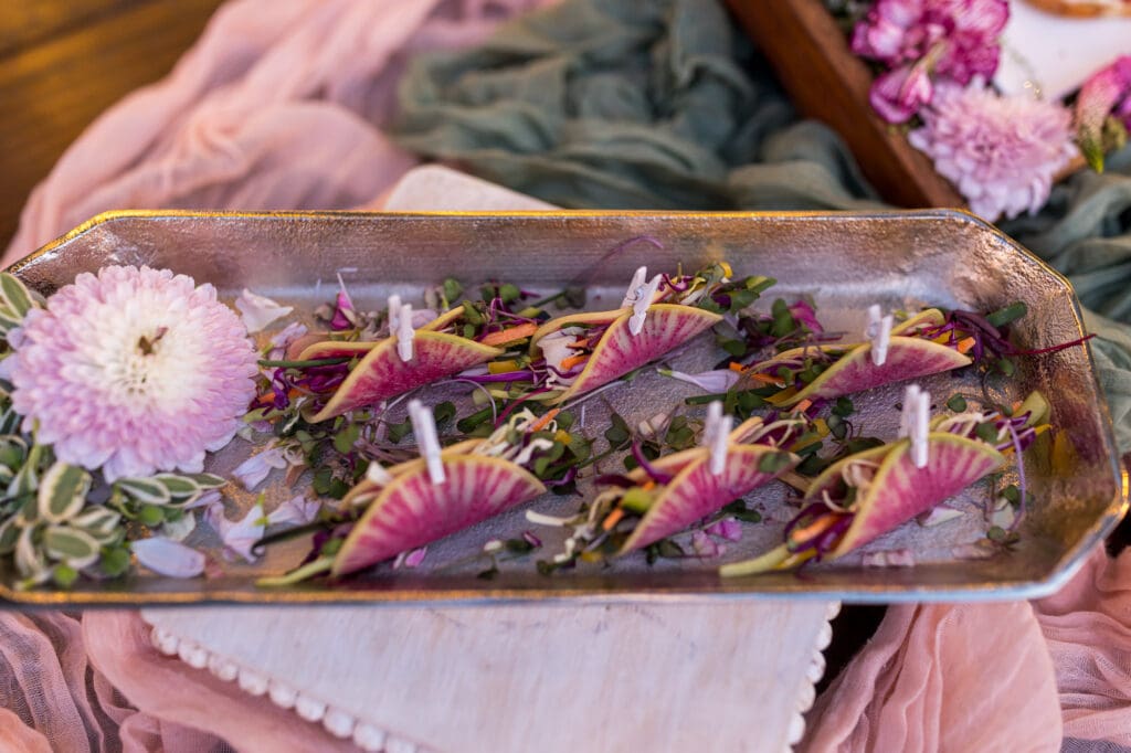 Mini tacos made with watermelon radish shells, filled with colorful microgreens and vegetables, displayed on a silver tray.